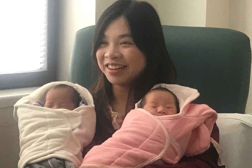 A new mother sitting in a chair smiling with her newborn twins