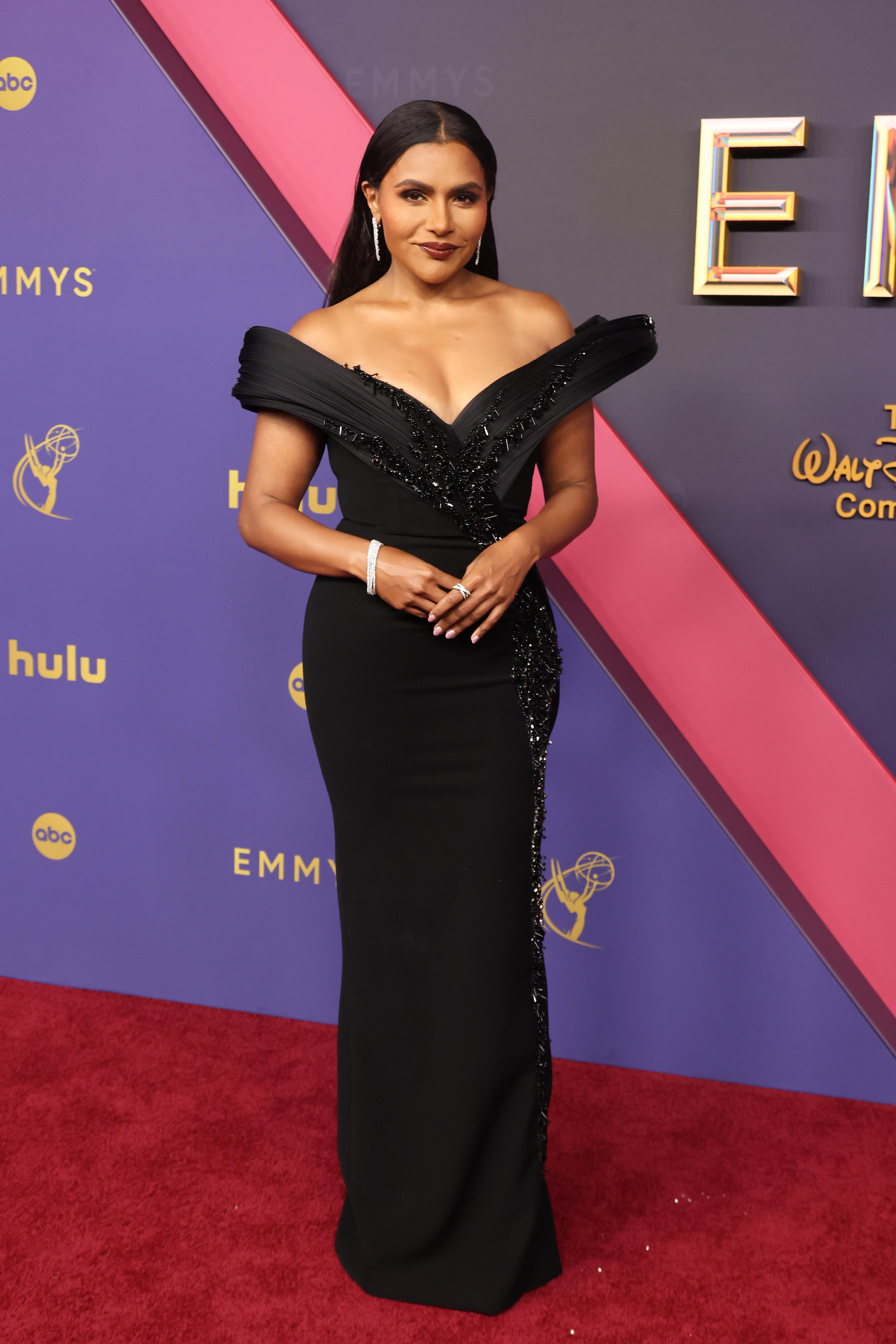 Mindy Kaling wearing a black floor-length off-the-shoulder gown with one strap extending wide