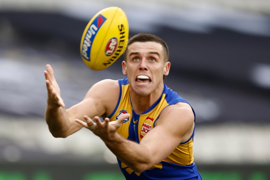 An Australian rules football player prepares to catch the ball.