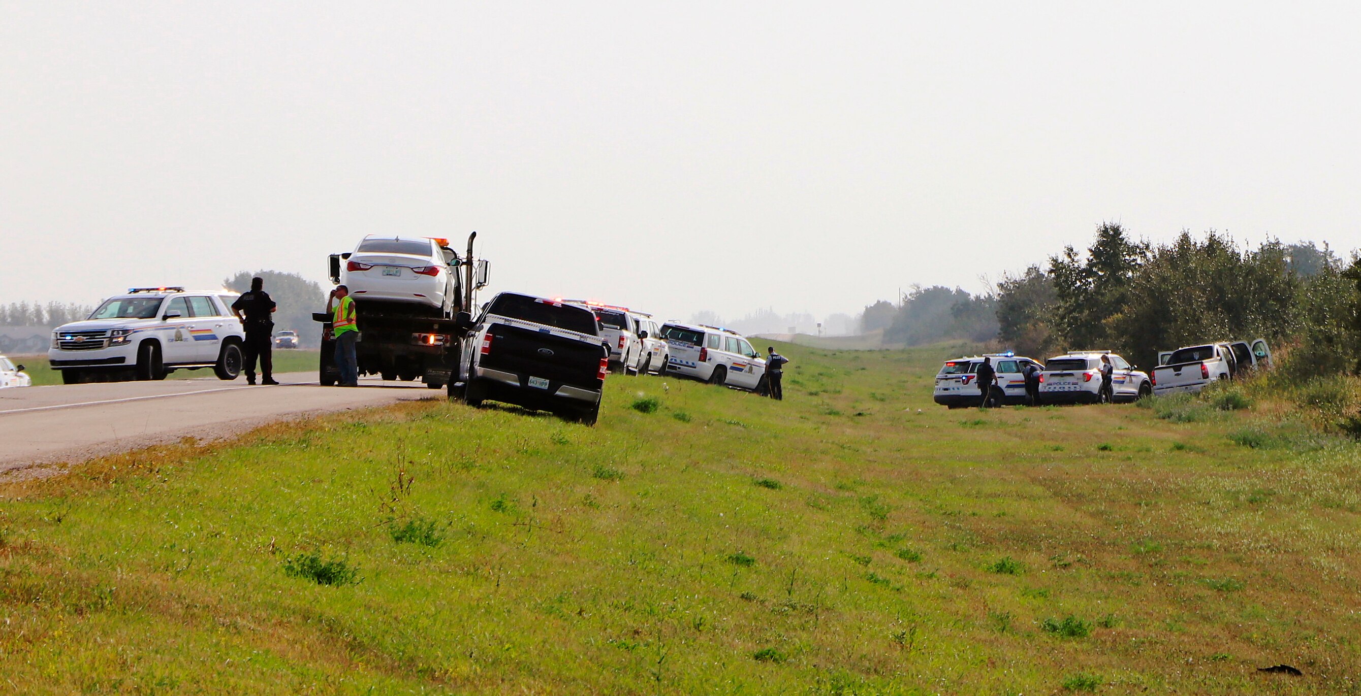 A large SUV in an embankment next to a road, with its doors open and police cars and police officers nearby.