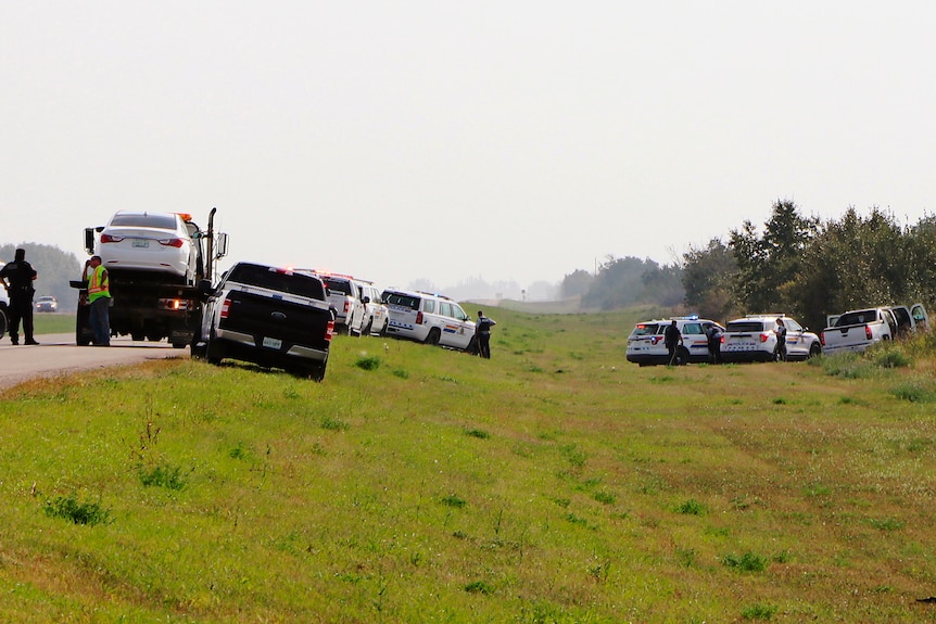 A large SUV in an embankment next to a road, with its doors open and police cars and police officers nearby.