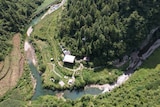 A bird's-eye view of a cottage nestled at the base of the mountains next to a river in China.