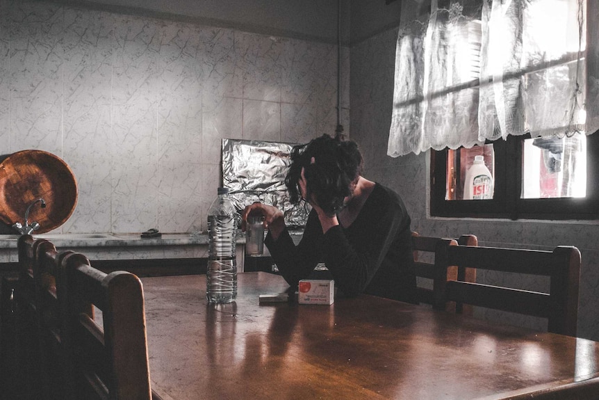 Woman holding head in hands at kitchen table and experiencing feelings of failure.