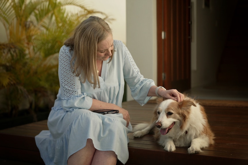 Jo O'Halloran sits on a wooden deck, patting a fluffy dog.