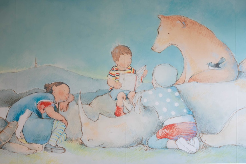 A young child reads a story in the mural, to two other children and some animals, Black Mountain Tower in the background.