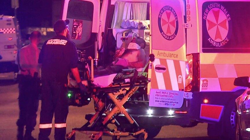 Paramedics load a man on a stretcher into an ambulance at night.