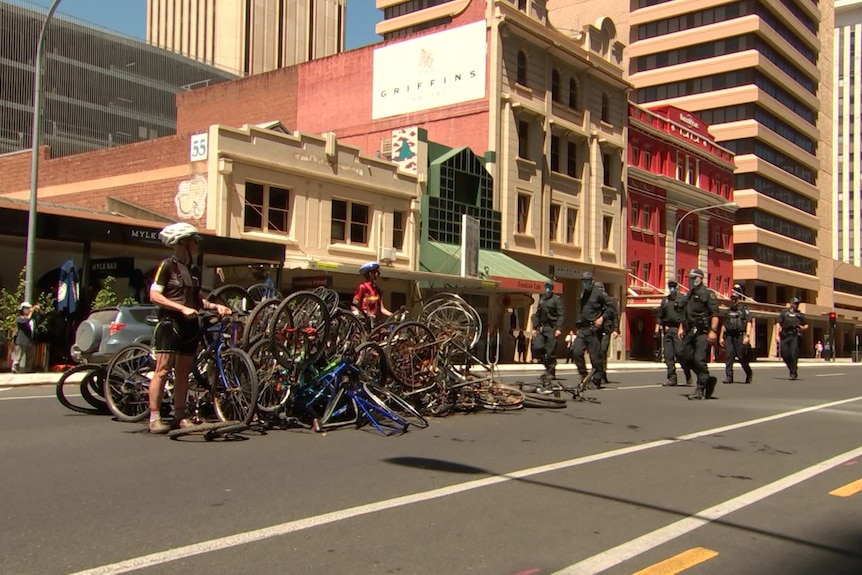 Two women stand among a group of bikes on a city street with police walking up to them