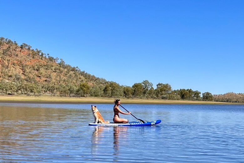 dog on paddle board with woman on lake