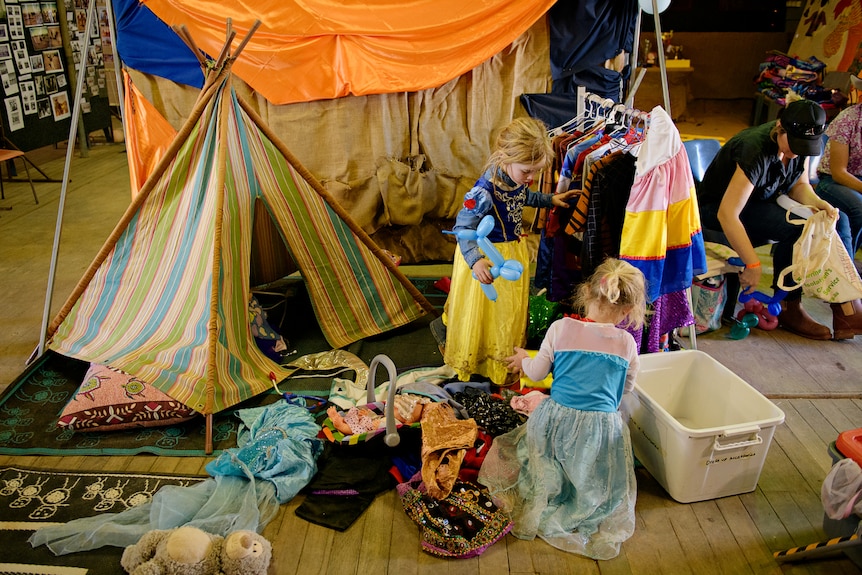 Two little girls playing dress-ups inside a large room.