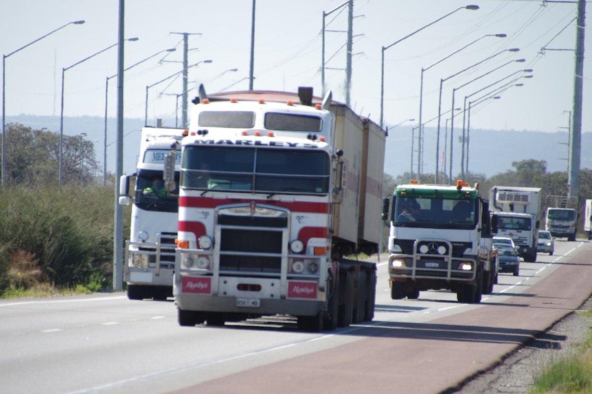 Three trucks on a highway, street lamps beside the road, overcast sky.