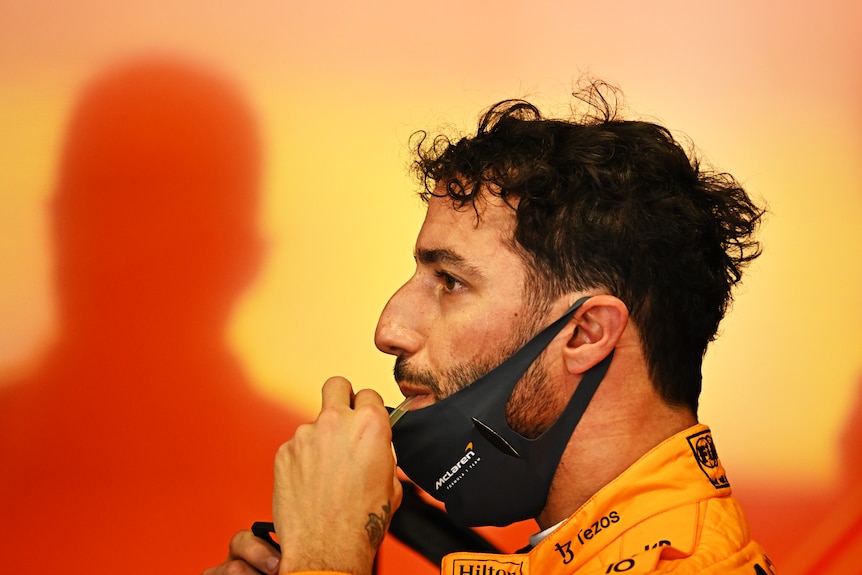 Racing driver in his racing suit drinking water in the garage.