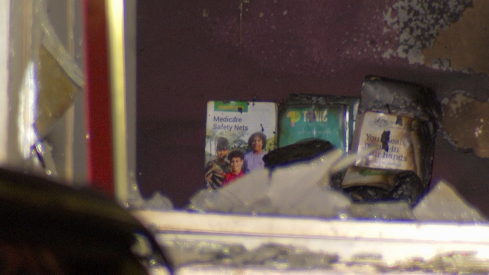 A smashed window with burnt medical flyers inside the store.