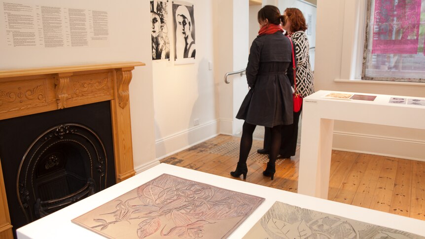 Two women look at a print by Joshua Searson, with a vinyl carving by Christobel Kelly in the foreground.