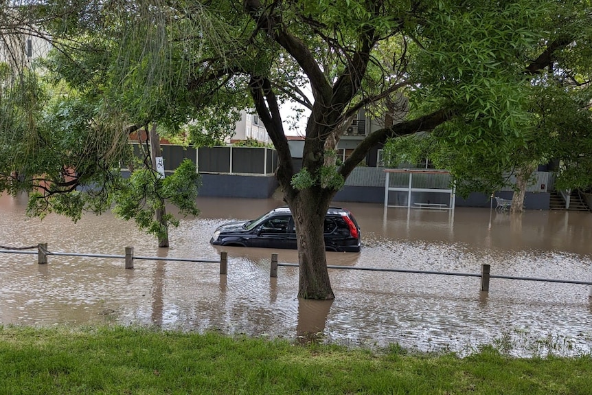 A car sits half-submerged in flood waters in a street