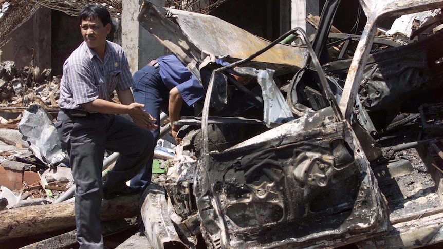 Indonesian police forensic experts examine a destroyed car in Bali amid the bomb wreckage in 2002