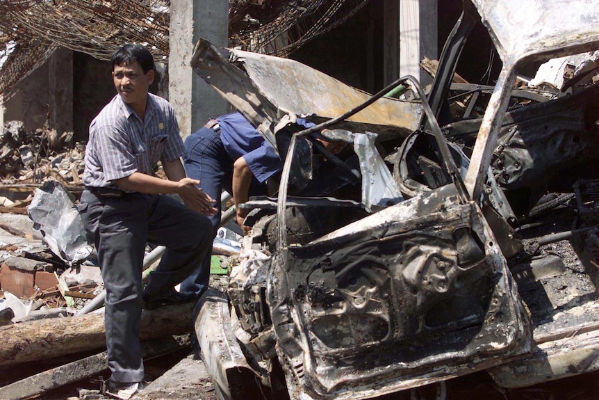 Indonesian police forensic experts examine a destroyed car in Bali amid the bomb wreckage in 2002
