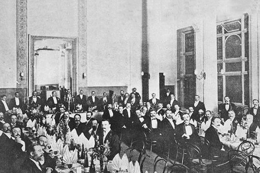 A black and white photo of a group of men seated around long tables