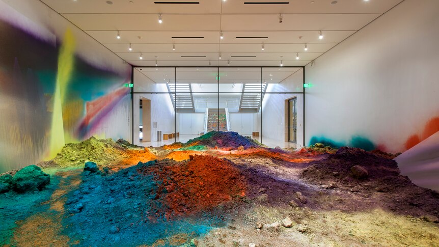 Gallery space filled with soil, and soil and walls of gallery have been spray-painted different bright colours.