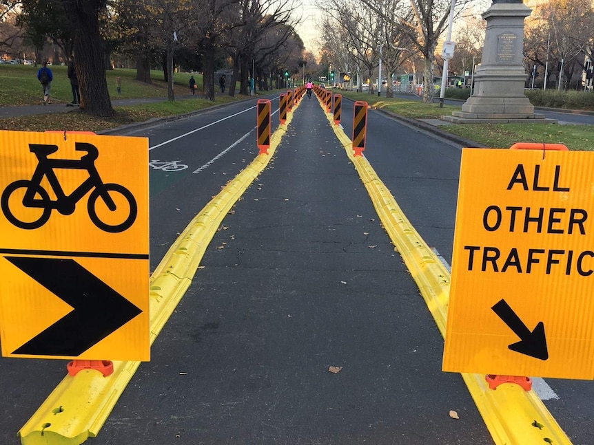 Yellow bollards reduce St Kilda Rd to one lane, as two signs direct motorists and cyclists.