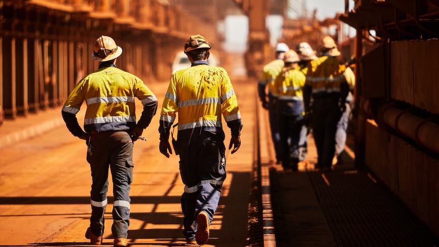 Mine workers in high-vis outfits walking away from camera, along what looks like a loading dock