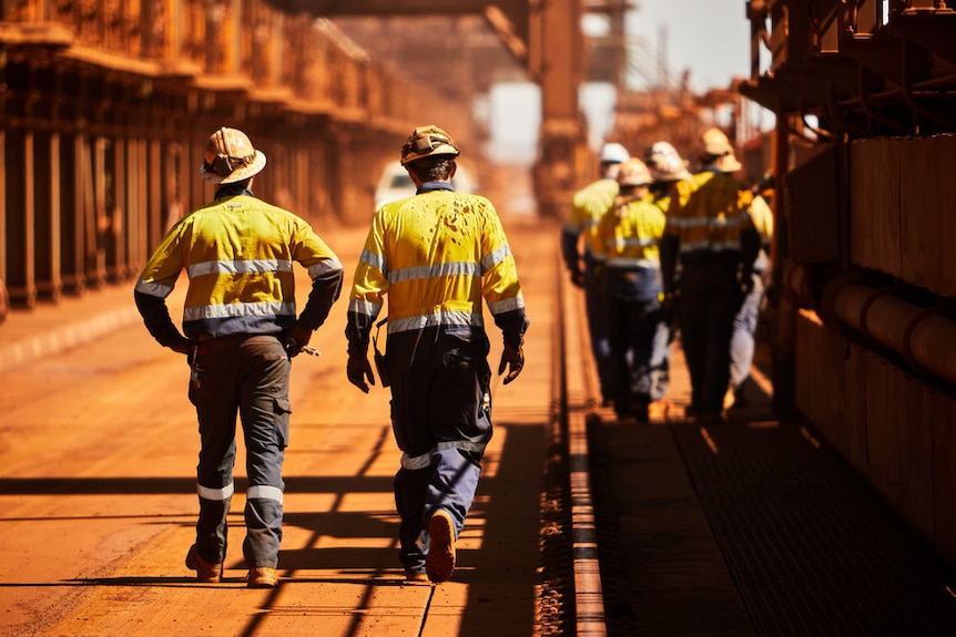 Men in high-vis and safety helmets walk through an industrial site.