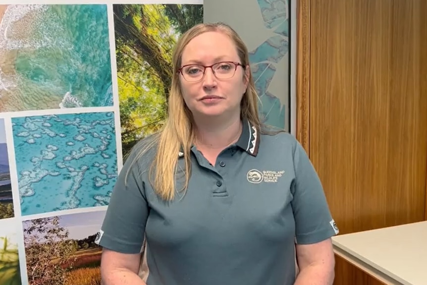 A bespectacled woman with long, blonde hair, wearing a branded polo shirt and standing in an office.