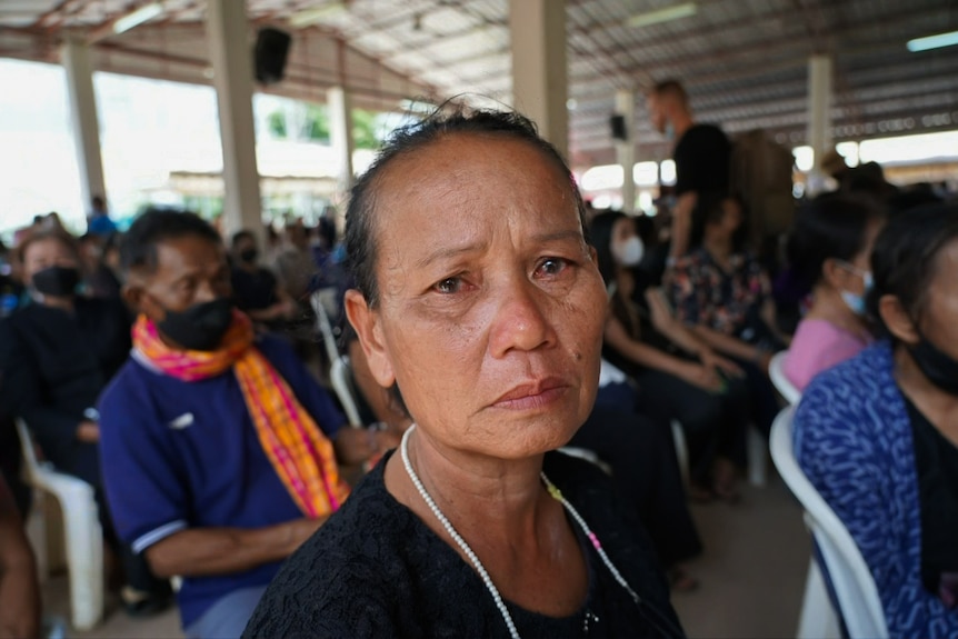 A woman's eyes are red and filled with tears as she looks towards camera in a hall full of people