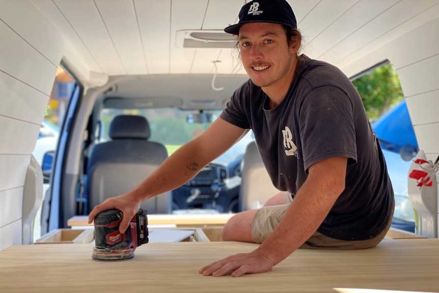 Man sitting in back of van holding an electric sander.