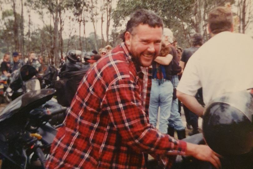 Old photo of Robert Piper as a younger man in a flannelette shirt at a motorbike meetup.