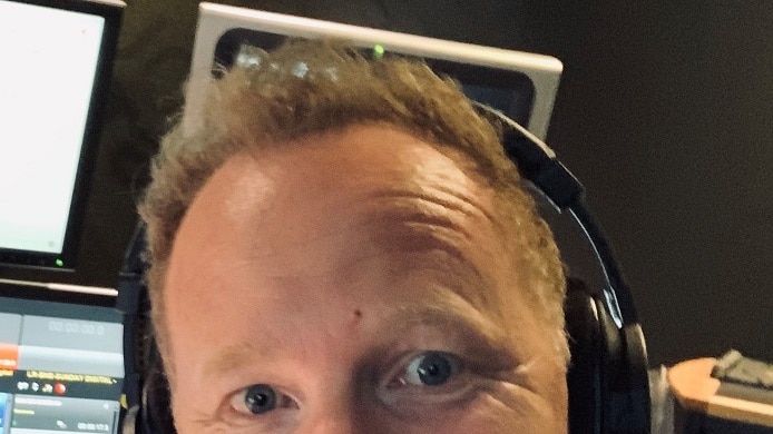 a smiling man wearing headphones in a radio studio
