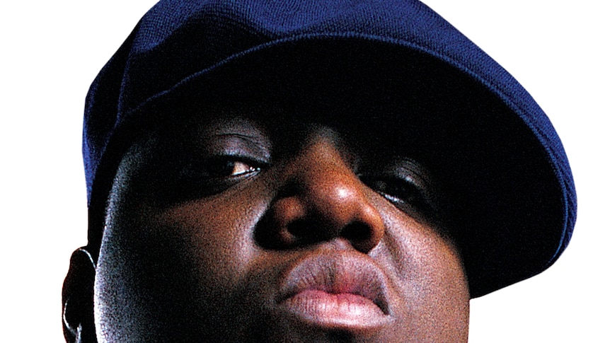 A close-up photo of the Notorious B.I.G.'s face. He wears a blue kangol style cap.