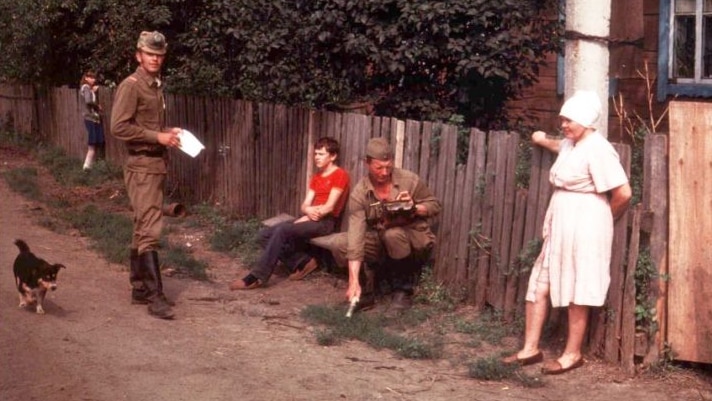 Two soldiers stand near a woman, two children and a small dog.