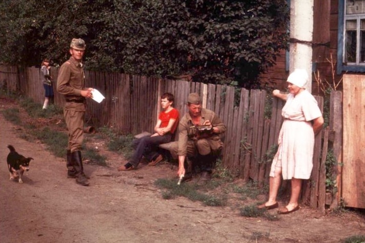 Two soldiers stand near a woman, two children and a small dog.