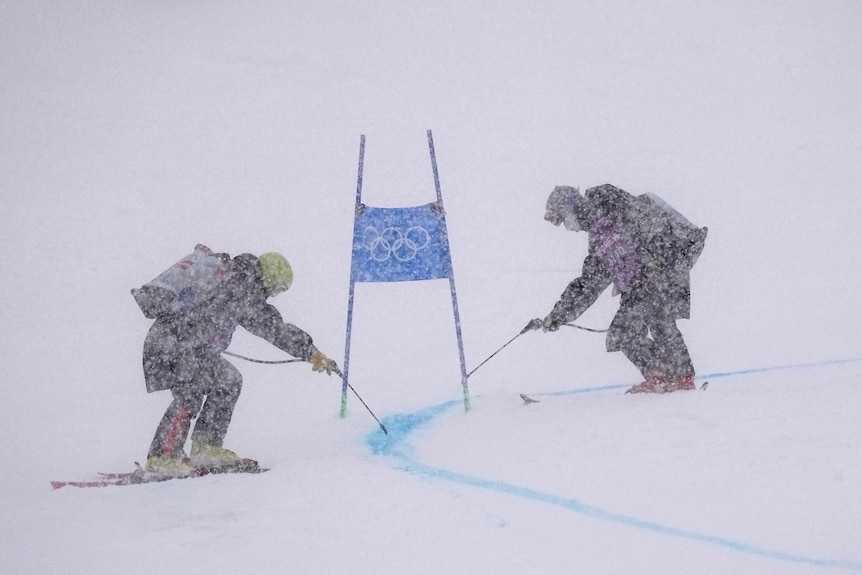 Two men spray lines on course in heavy snow.