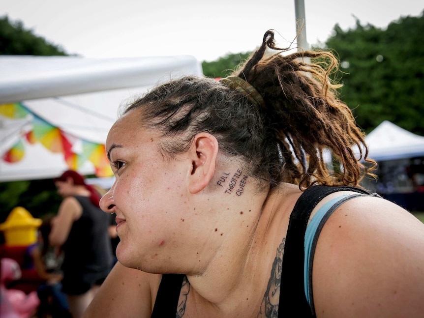 Jac turns her head to show off her new tattoo behind her ear, which reads "Full Throttle Queen"