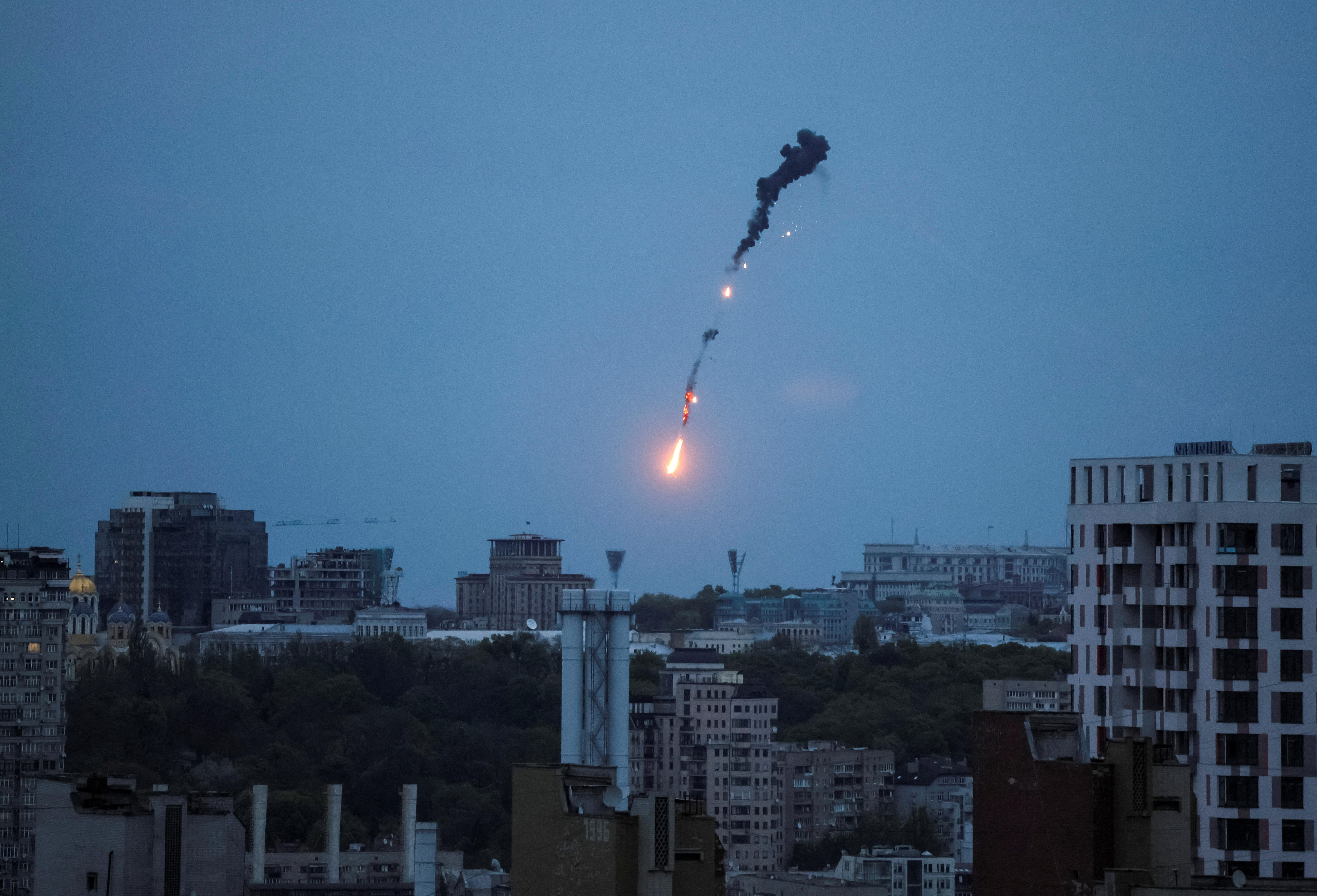 An exploding object is seen against a pale blue sky over the city at twilight