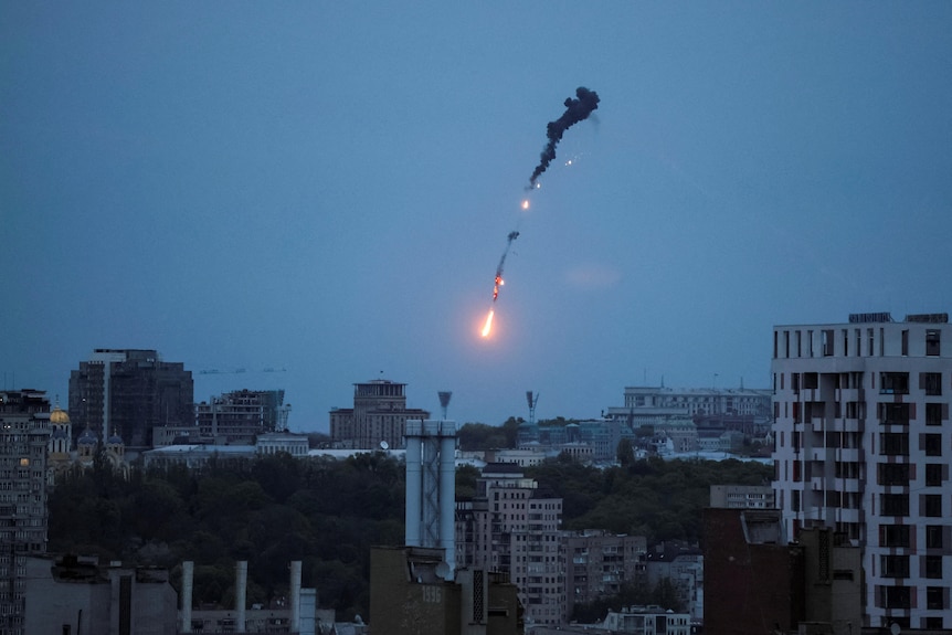 An exploding object is seen against a pale blue sky over the city at twilight
