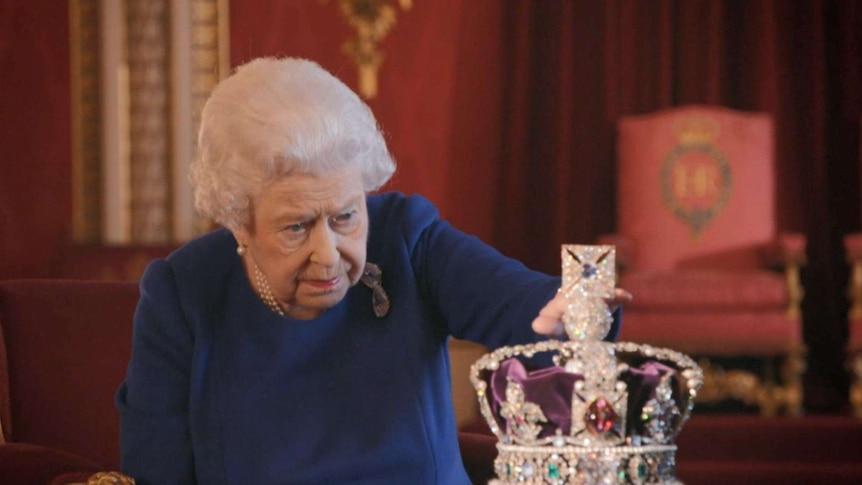 Queen Elizabeth II looks intently at the diamond encrusted Imperial State Crown and lightly touches the top.
