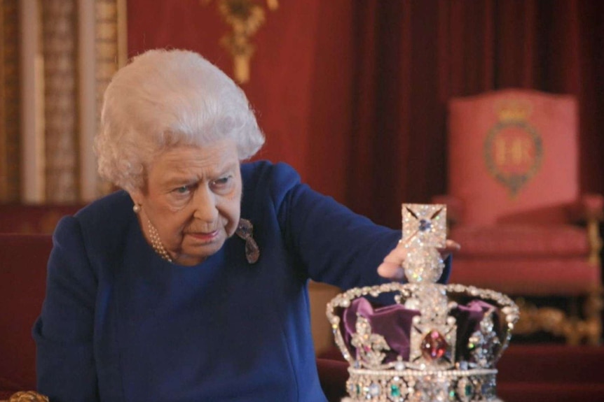 Queen Elizabeth II looks intently at the diamond-encrusted Imperial State Crown and lightly touches the top.