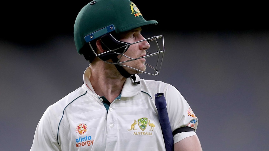 Cameron Bancroft looks to the side with his bat tucked under his arm and his batting helmet on