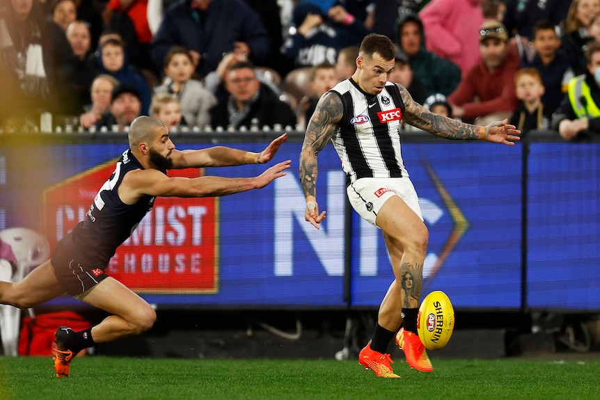 A Collingwood AFL player kicks the ball on the run as a Carlton player makes a despairing dive to stop him.