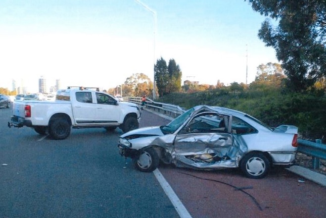 A wide shot showing two crashed cars, a silver sedan and a white ute, on the Mitchell Freeway, with the sedan's side stowed in.