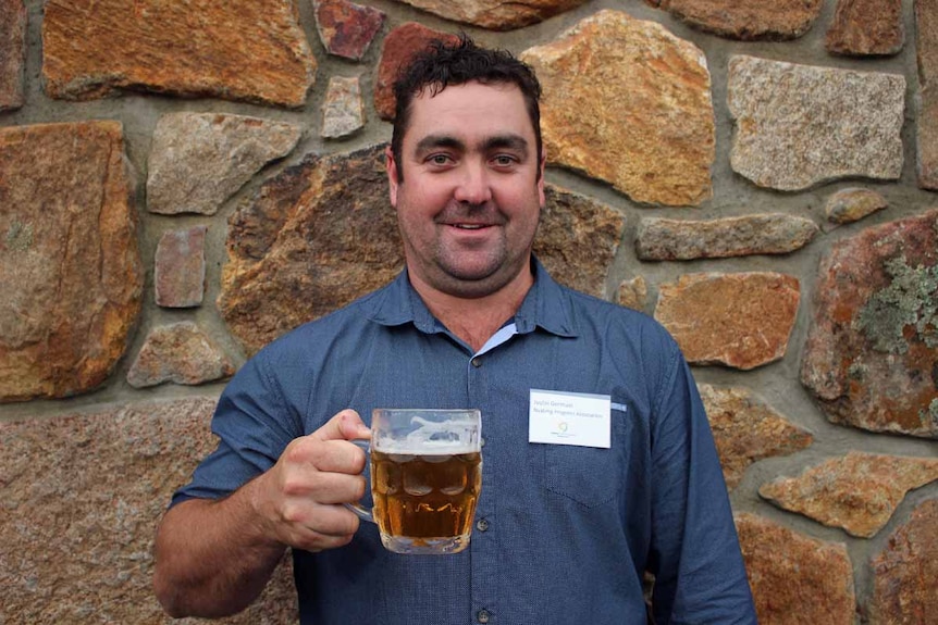 A man stands in front of a rock wall holding a glass of beer.