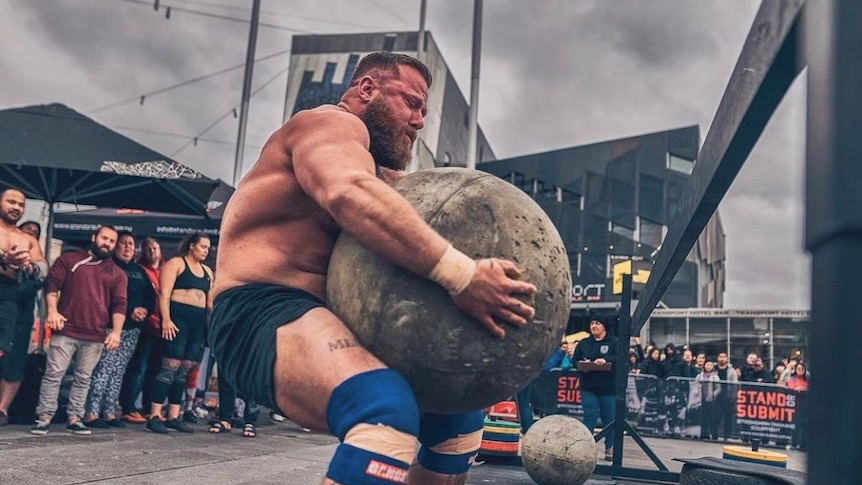 Strongman competitor Tyson Morrissy lifting a huge sphere of concrete