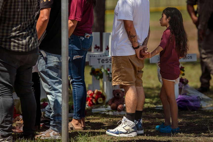 A young person holds onto an adults hand as they visit a memorial