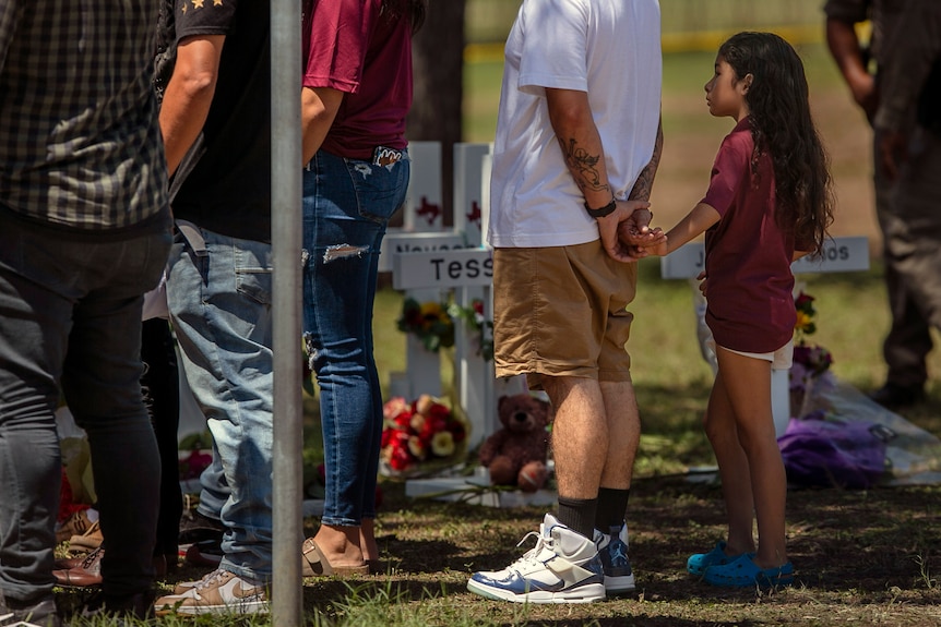 A young man holds an adult's hand as he visits a memorial