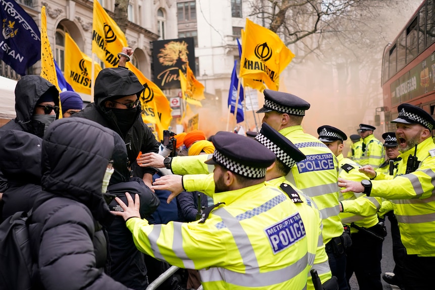 Police in high-vis jackets push a crowd of people in winter coats, with yellow KHALISTAN flags