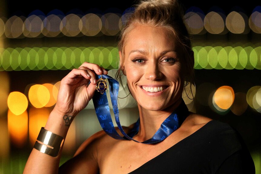 Erin Phillips smiles while holding the medal next to her face.