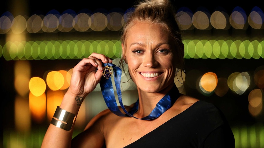 Erin Phillips smiles while holding the medal next to her face.