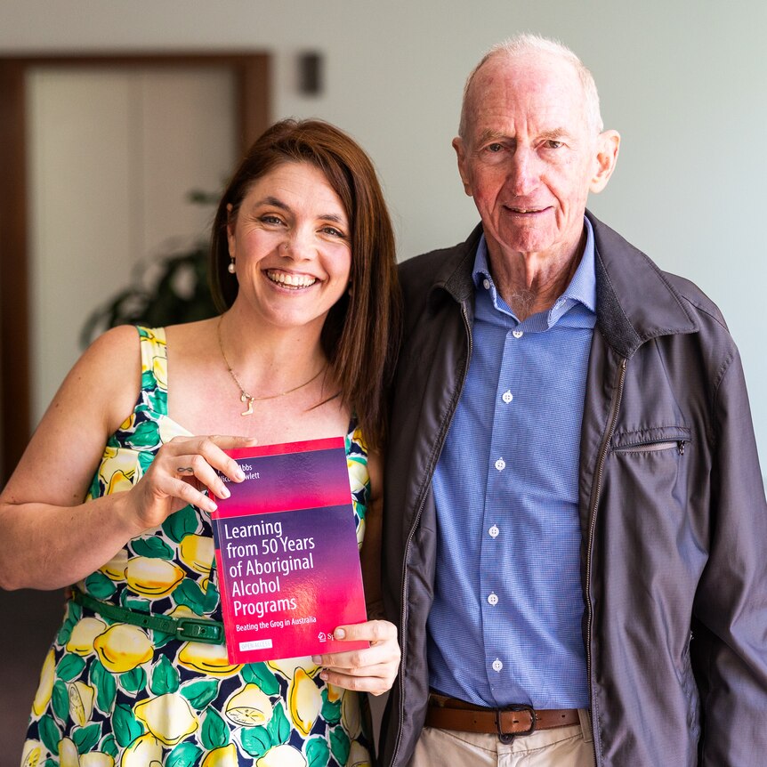 A smiling woman and man standing together holding their publication